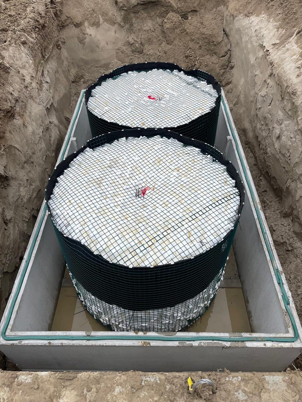 Two cylindrical tertiary treatment filter units set inside a concrete tank in the ground