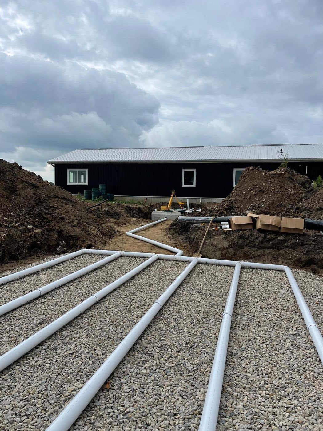 Septic distribution laterals on clear stone in front of a large dark agricultural building