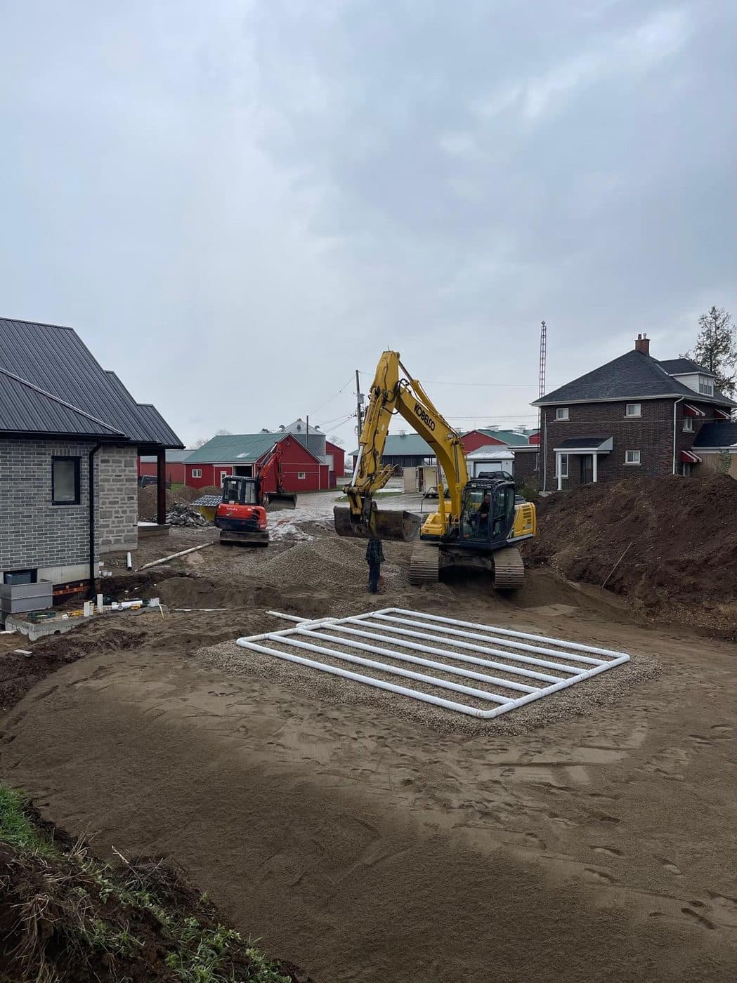 Excavators working a septic installation on a rural farm property, with a distribution bed on stone