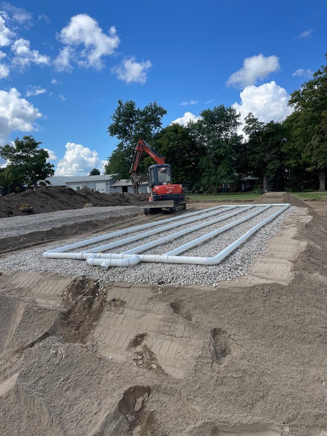 Completed septic distribution bed on clear stone with an excavator on a Southern Ontario job site